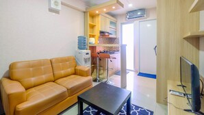 A living room with a sofa and a coffee table, a kitchen area with a sink and stools, and a TV on a wooden stand. - Nice and Strategic 2BR at Bassura City Apartment (Jakarta)