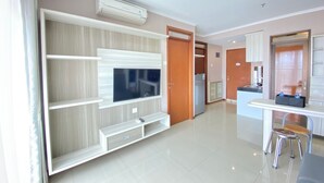 A modern living room with a flat-screen TV, built-in shelves, and a dining area with a kitchen in the background.