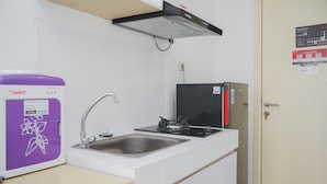 A small kitchenette with a sink, a purple water dispenser, a black stove, and a door with a fire safety sign.