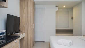 A modern hotel room with a flat-screen TV, wooden wardrobe, white bed, and a staircase leading to an upper level. - Nice and Cozy Studio at Baileys Apartment (South Tangerang)