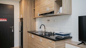 A modern kitchen with wooden cabinets, a black countertop, a stove, a sink, and a television. - Nice and Cozy Studio at Baileys Apartment (South Tangerang)