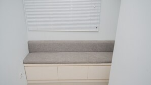 A neutral-colored bench with storage drawers underneath, against a plain wall with a window above. - Nice and Cozy Studio at Baileys Apartment (South Tangerang)