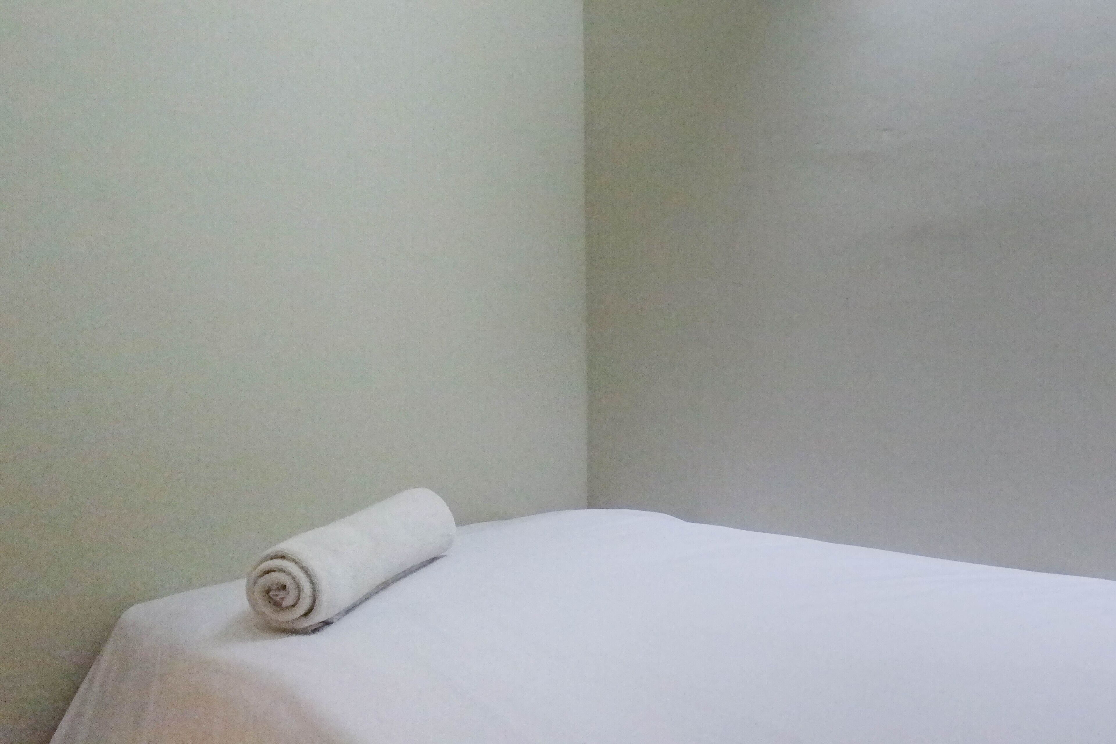A neatly made bed with a rolled white towel on the side.