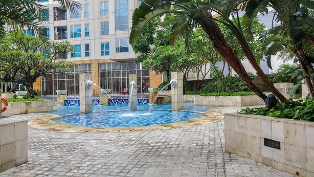 A swimming pool with water features, surrounded by greenery and a modern building in the background.