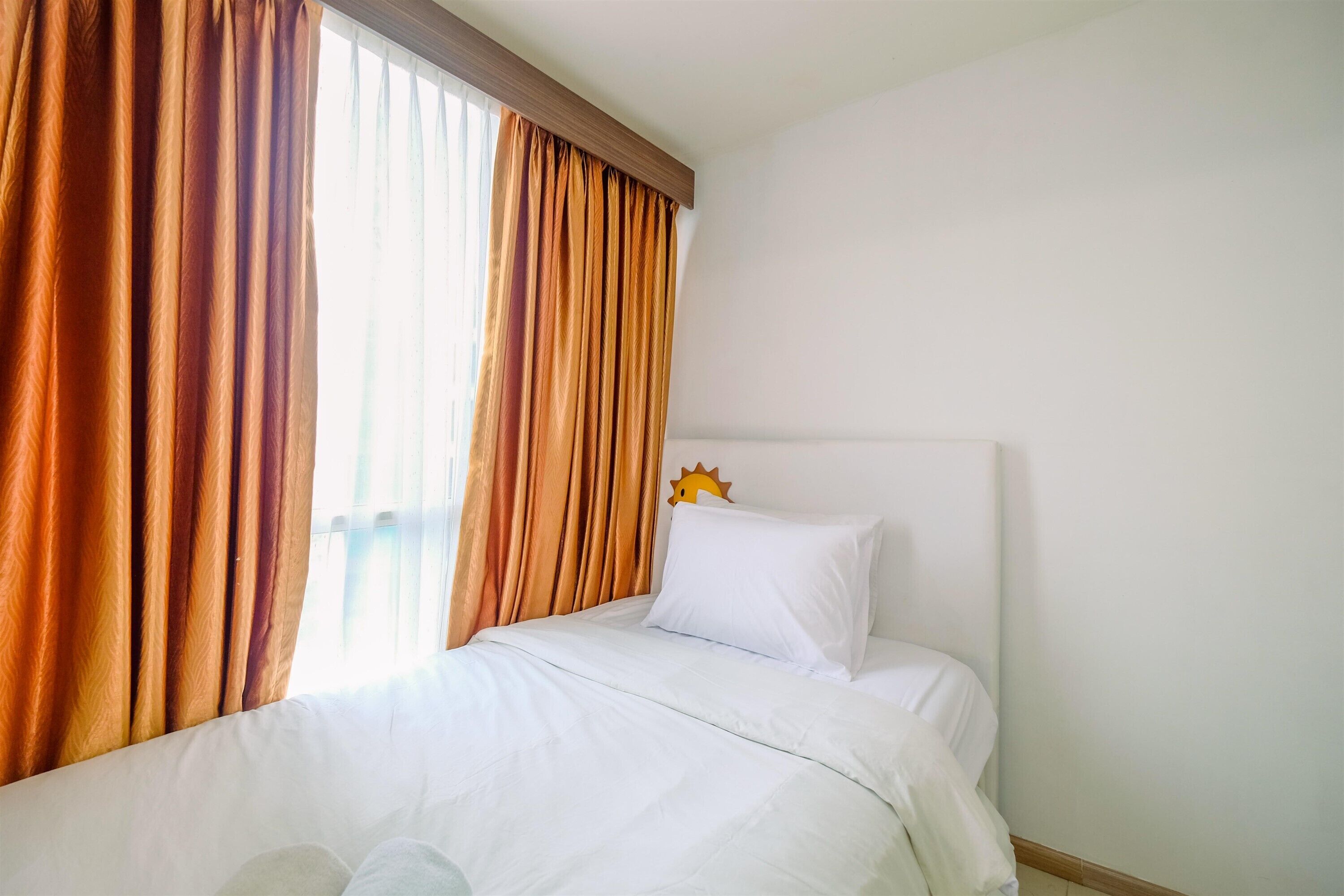 A hotel room with a bed, white bedding, a window with curtains, and a sun-shaped decoration on the wall.
