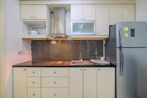 A kitchen with white cabinets, a stainless steel range hood, a microwave, and a refrigerator.