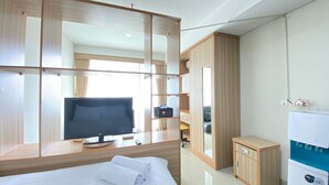 A hotel room with a bed, a TV, a minibar, and a water dispenser. - Stylish & Comfy Studio at Dago Suites Apartment (Bandung)