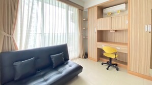 A modern living room with a dark sofa, a yellow office chair, and a wooden wardrobe with built-in shelves. - Stylish & Comfy Studio at Dago Suites Apartment (Bandung)