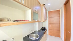 A modern kitchen with wooden cabinets, a black countertop, a stainless steel sink, and a microwave. - Stylish & Comfy Studio at Dago Suites Apartment (Bandung)