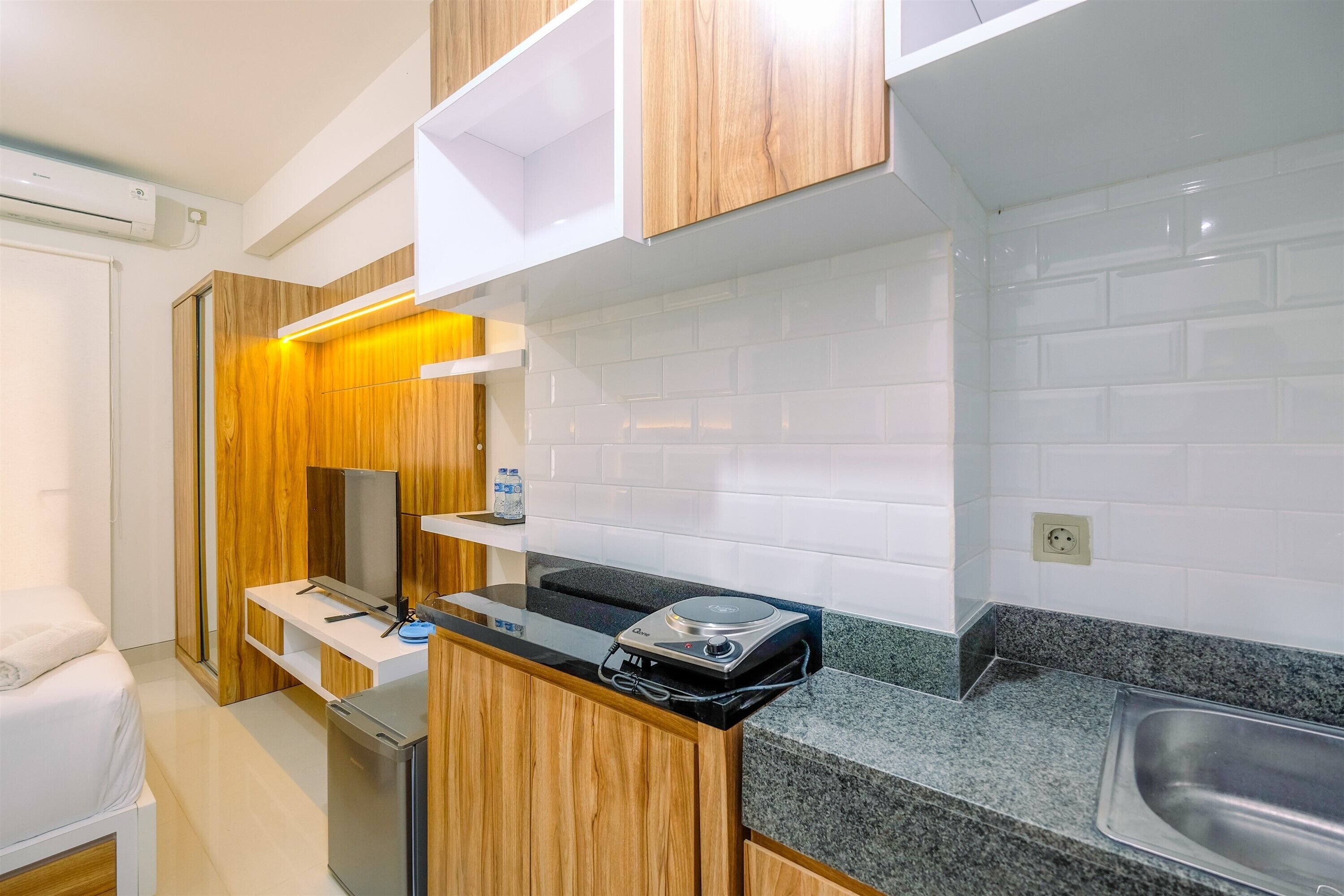 Una kitchenette compacta equipada con estufa integrada, un refrigerador pequeño y un lavamanos en la encimera.