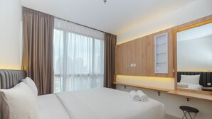 Habitación de hotel moderna con una cama grande, una mesita de noche con lámpara, un espejo y vistas a la ciudad a través de amplios ventanales.