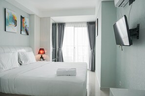 Habitación de hotel con una cama grande, una lámpara de noche, un televisor de pantalla plana en la pared y una ventana con cortinas.