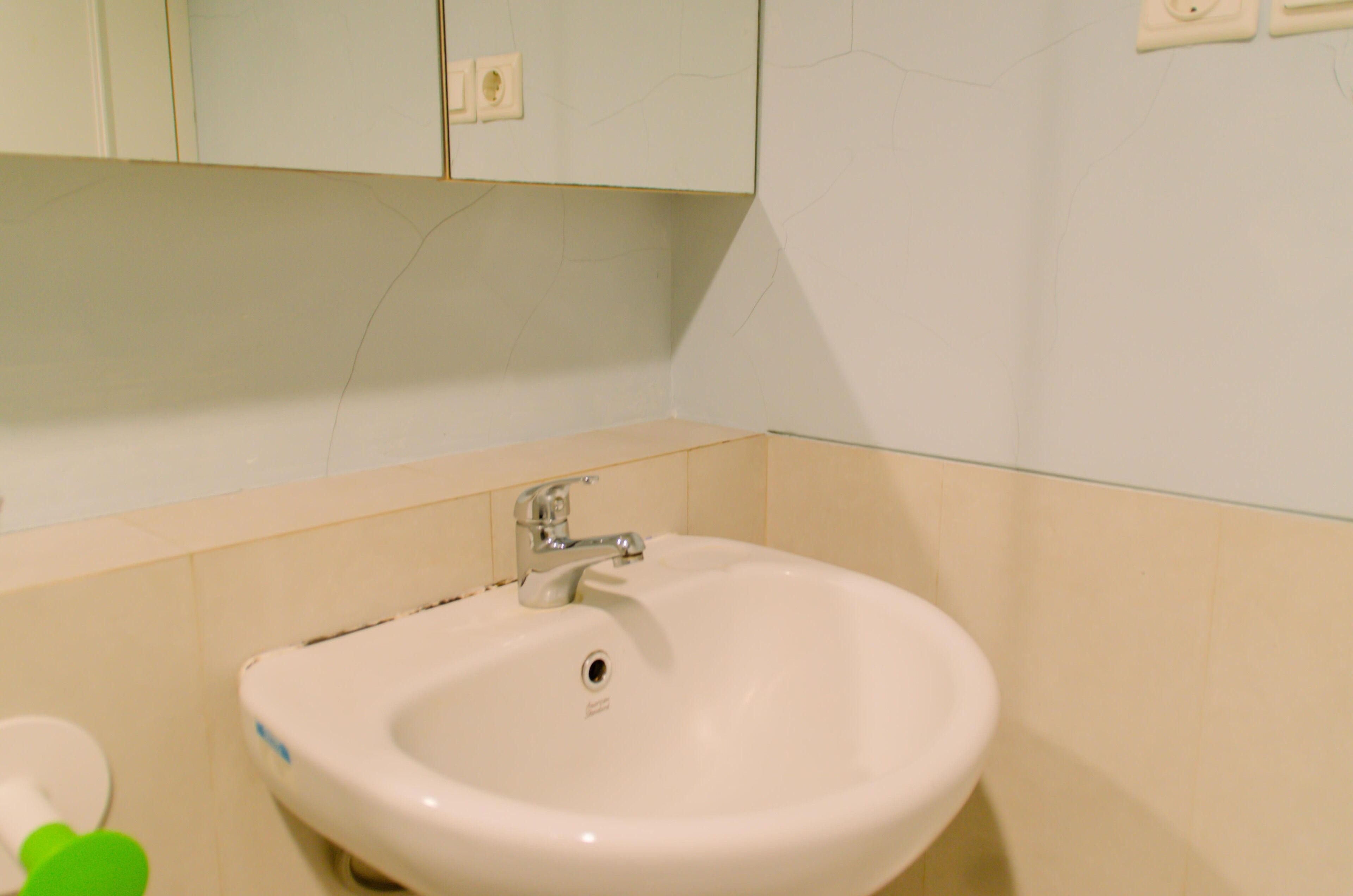 A bathroom with a white sink, a mirror above it, and a green object on the floor.