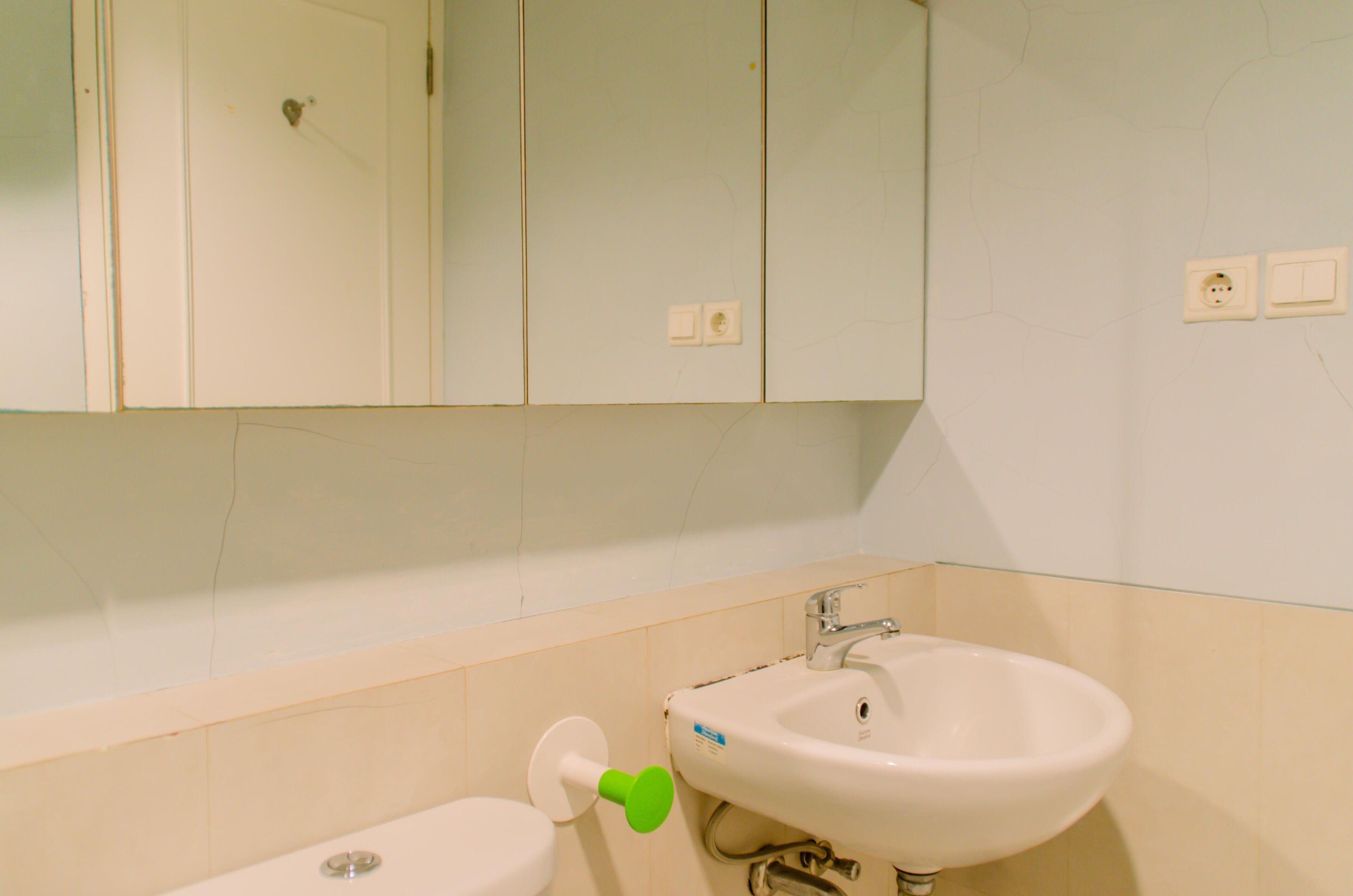 Un baño con un lavamanos blanco, un dispensador de papel higiénico verde y un espejo sobre el lavamanos.