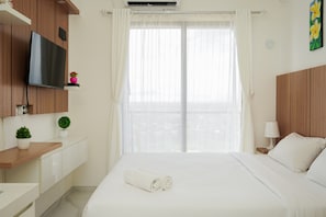 A hotel room with a bed, a TV mounted on the wall, a small potted plant, and a window with curtains. - Well Appointed and Homey Studio at Sky House BSD Apartment (Pagedangan)