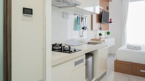 Cocina compacta con estufa, lavabo y un refrigerador pequeño. Hay un gabinete de madera sobre la encimera y un televisor montado en la pared.