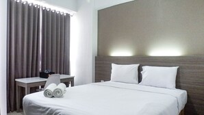 Quarto de hotel com uma cama, uma escrivaninha e uma cadeira. Há dois travesseiros na cama e um par de toalhas enroladas sobre ela.