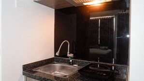Uma cozinha compacta com uma pia de aço inoxidável, uma torneira e um pequeno eletrodoméstico preto no balcão.