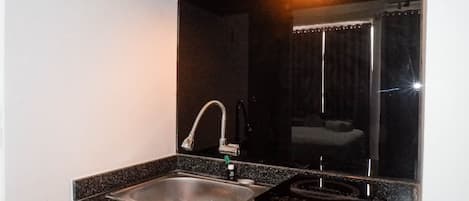 A compact kitchen with a stainless steel sink, a faucet, and a small black appliance on the counter.