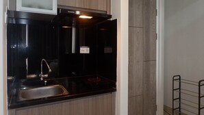 A modern kitchen with a black countertop, stainless steel sink, and wooden cabinets. - Chic and Cozy Studio Apartment at Taman Melati Surabaya (Surabaya)