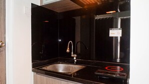 A modern kitchen with a black countertop, stainless steel sink, and a built-in stove with a red heating element. - Chic and Cozy Studio Apartment at Taman Melati Surabaya (Surabaya)