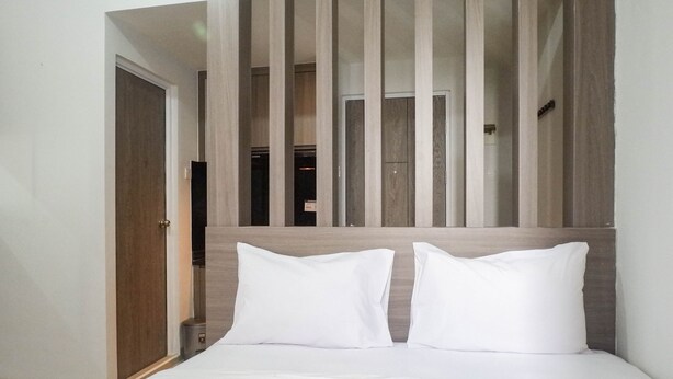 A modern hotel room with a large bed, wooden headboard, and a view of the hallway. - Chic and Cozy Studio Apartment at Taman Melati Surabaya (Surabaya)