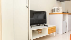 Una cocina moderna con un televisor de pantalla plana sobre un mueble blanco, una cafetera y un refrigerador pequeño.