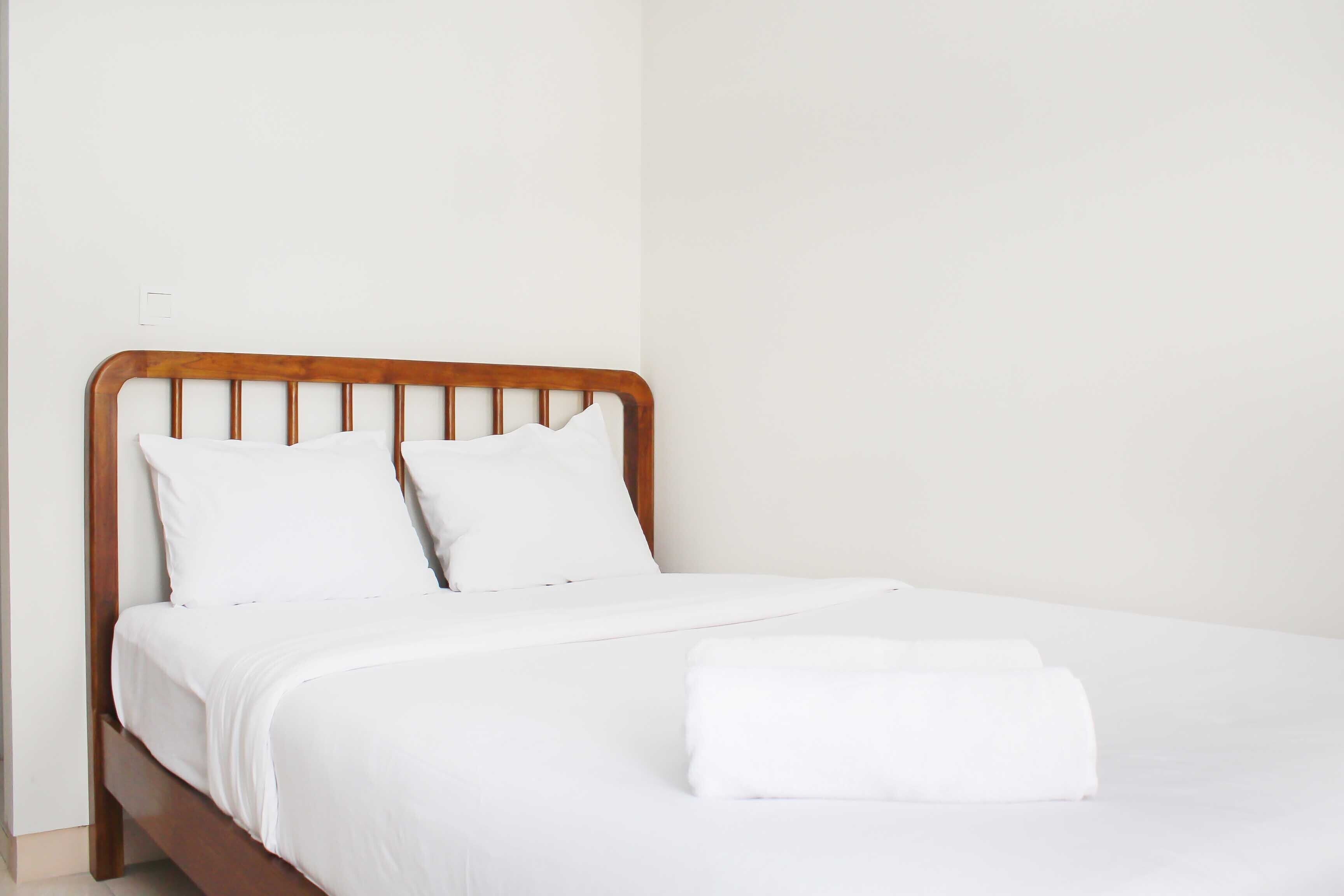 A neatly made bed with white linens and a wooden headboard.