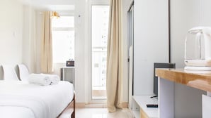 Una habitación de hotel con cama, escritorio, televisor y ventana con cortinas.