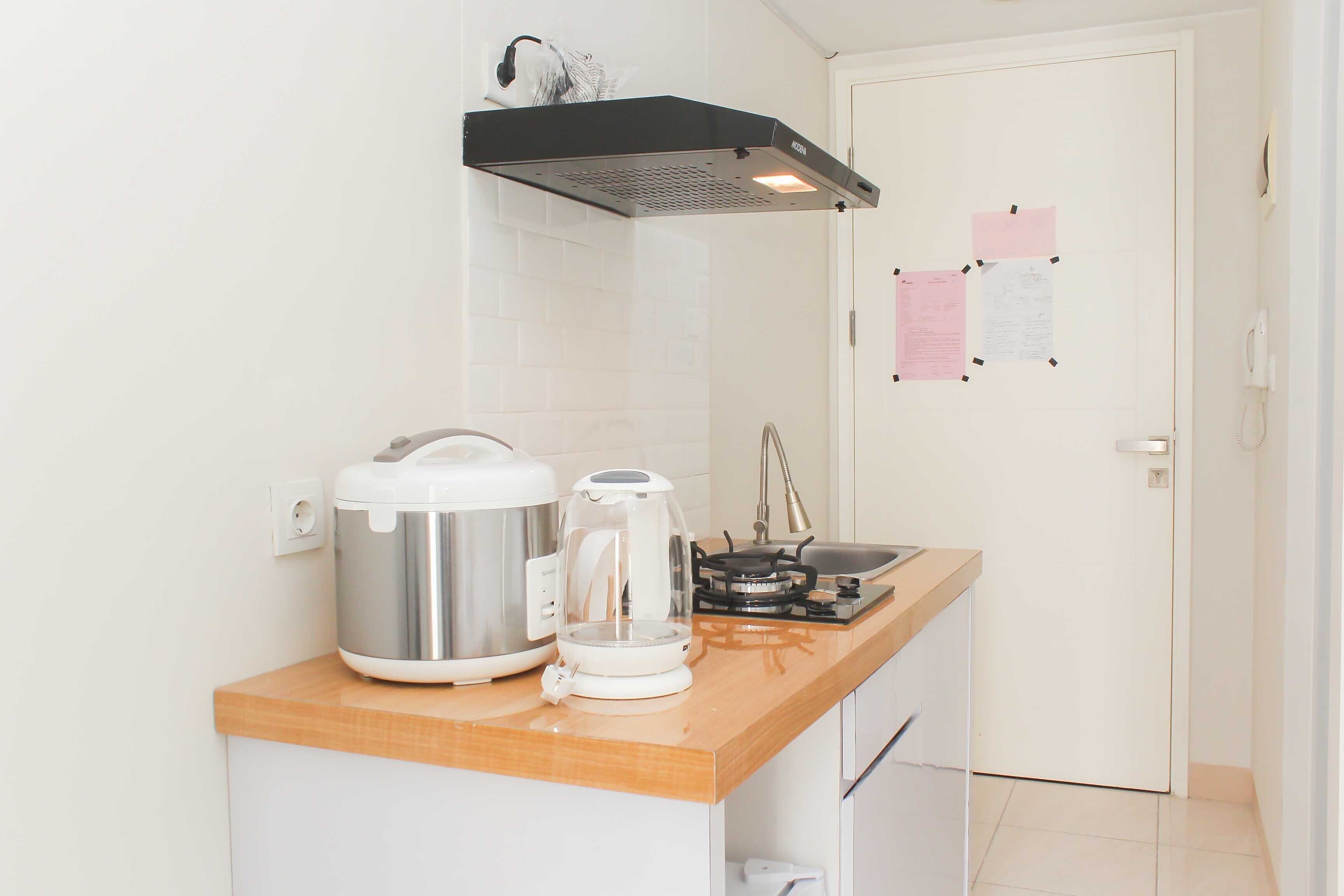 Una cocina compacta con una olla arrocera de acero inoxidable, una cafetera y una estufa a gas.