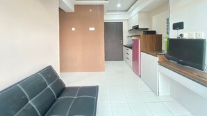 A modern living room with a black sofa, a kitchen area with a pink refrigerator, and a flat-screen TV on a wooden counter. - Roomy 2BR Apartment at Jarrdin Cihampelas Apartment (Bandung)