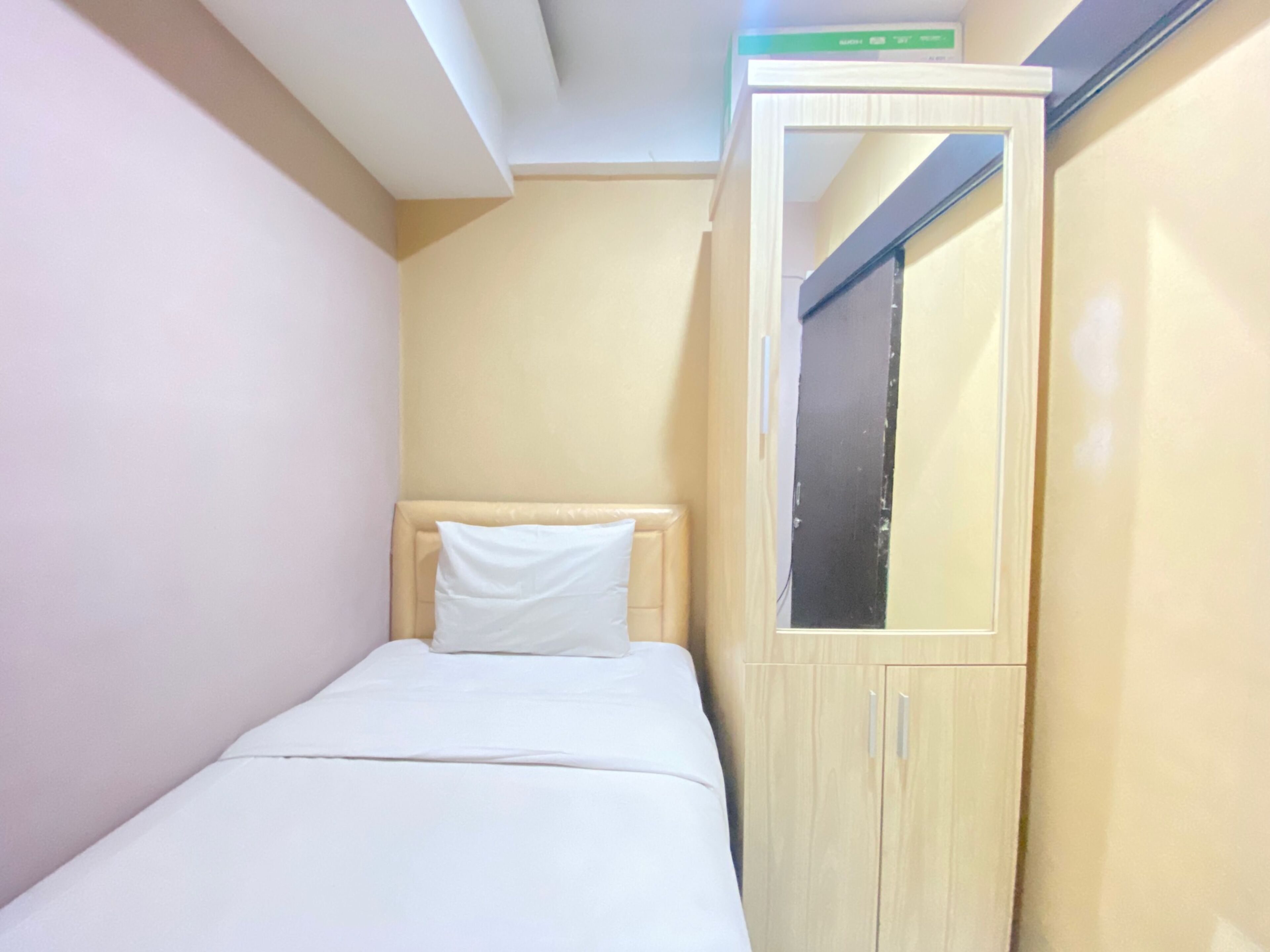 Una habitación pequeña con cama individual, armario de madera y espejo.