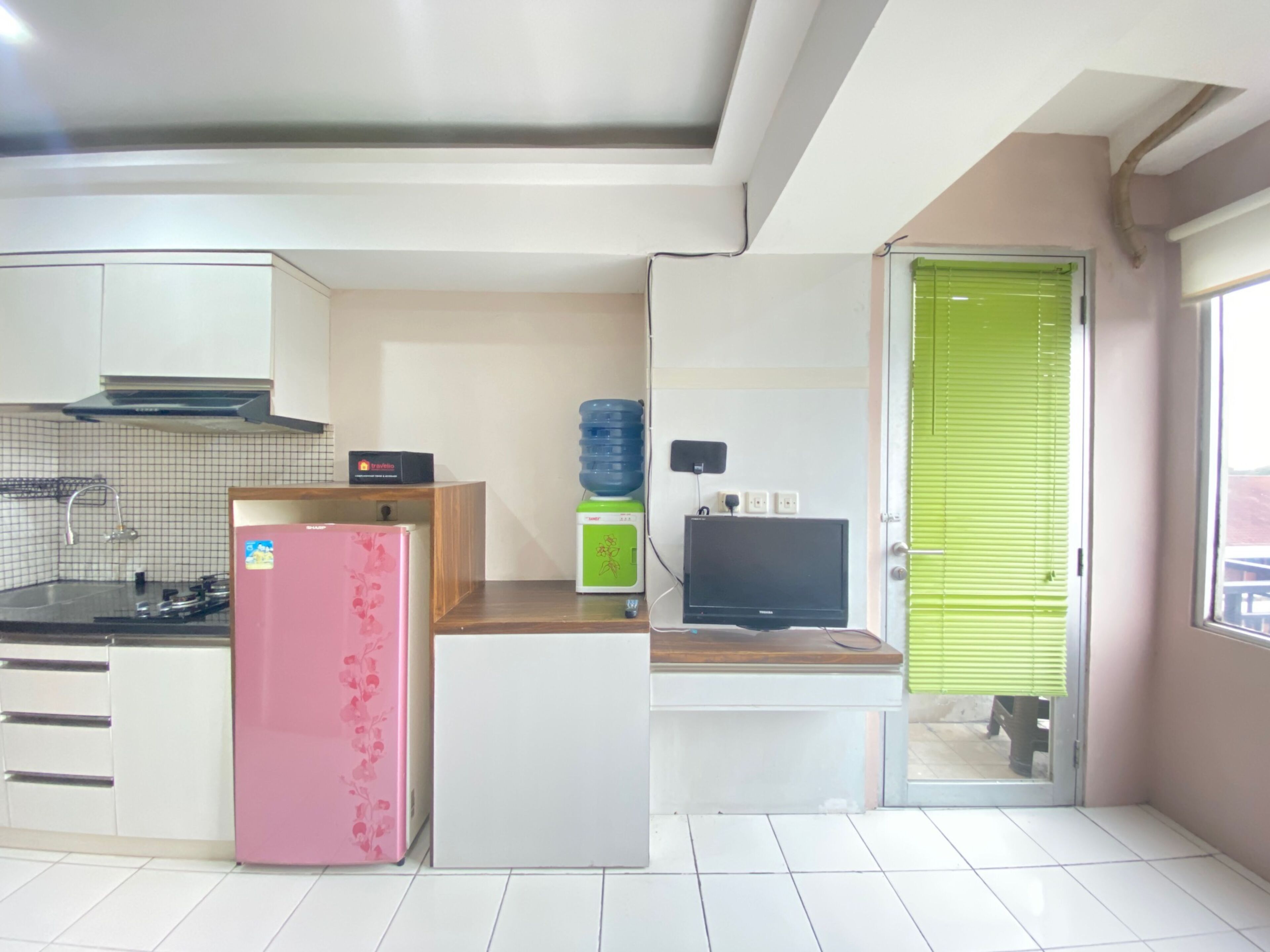 A modern kitchen with white cabinets, a pink refrigerator, a water dispenser, and a flat-screen TV.
