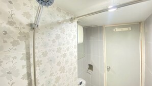 A bathroom with floral wallpaper, a shower with a handheld showerhead, and a toilet with a small shelf. - Roomy 2BR Apartment at Jarrdin Cihampelas Apartment (Bandung)
