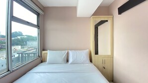 A hotel room with a large window, a bed with white linens, a wooden wardrobe, and a mirror on the wall. - Roomy 2BR Apartment at Jarrdin Cihampelas Apartment (Bandung)