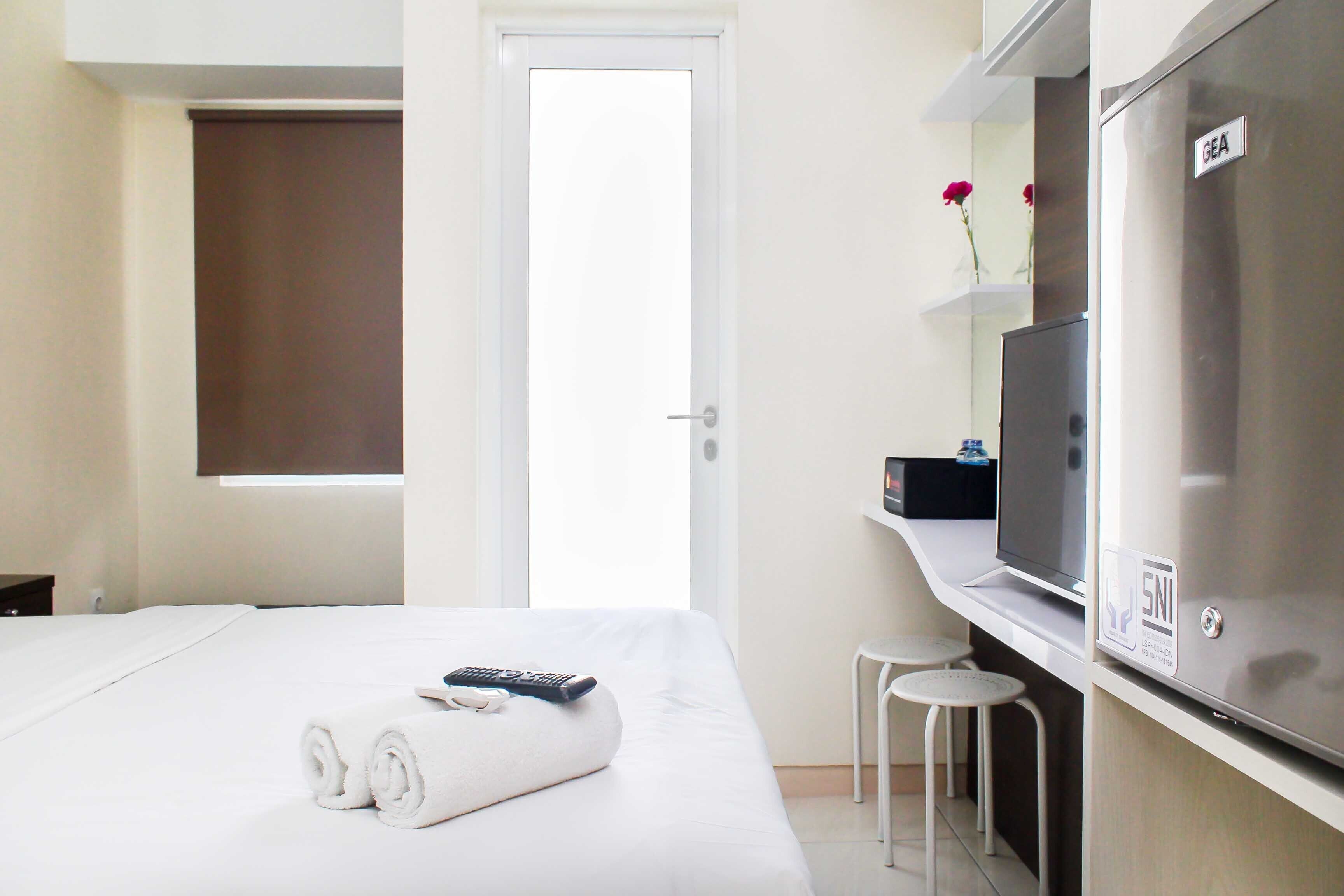 Een hotelkamer met een bed, televisie, minibar en een badkamedeur.