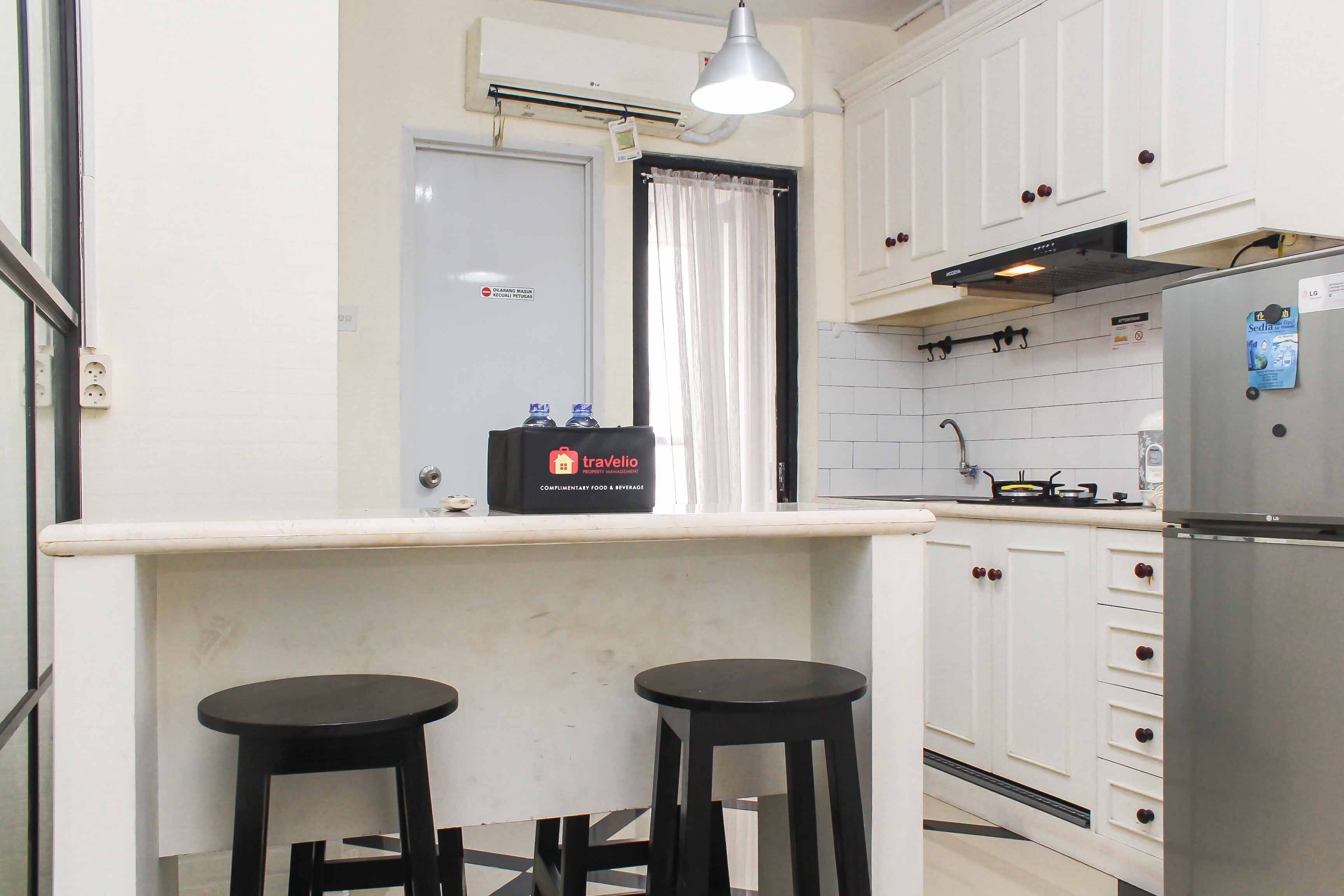 Una cocina pequeña con armarios blancos, un refrigerador de acero inoxidable y dos taburetes negros.