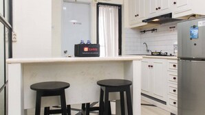 A compact kitchen with white cabinets, a stainless steel refrigerator, and two black stools. - White and Nice 1BR at Bassura City Apartment (Jakarta)