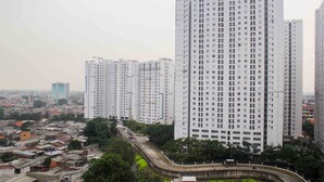 A high-rise residential building with multiple floors, a curved road in the foreground, and surrounding low-rise buildings. - White and Nice 1BR at Bassura City Apartment (Jakarta)
