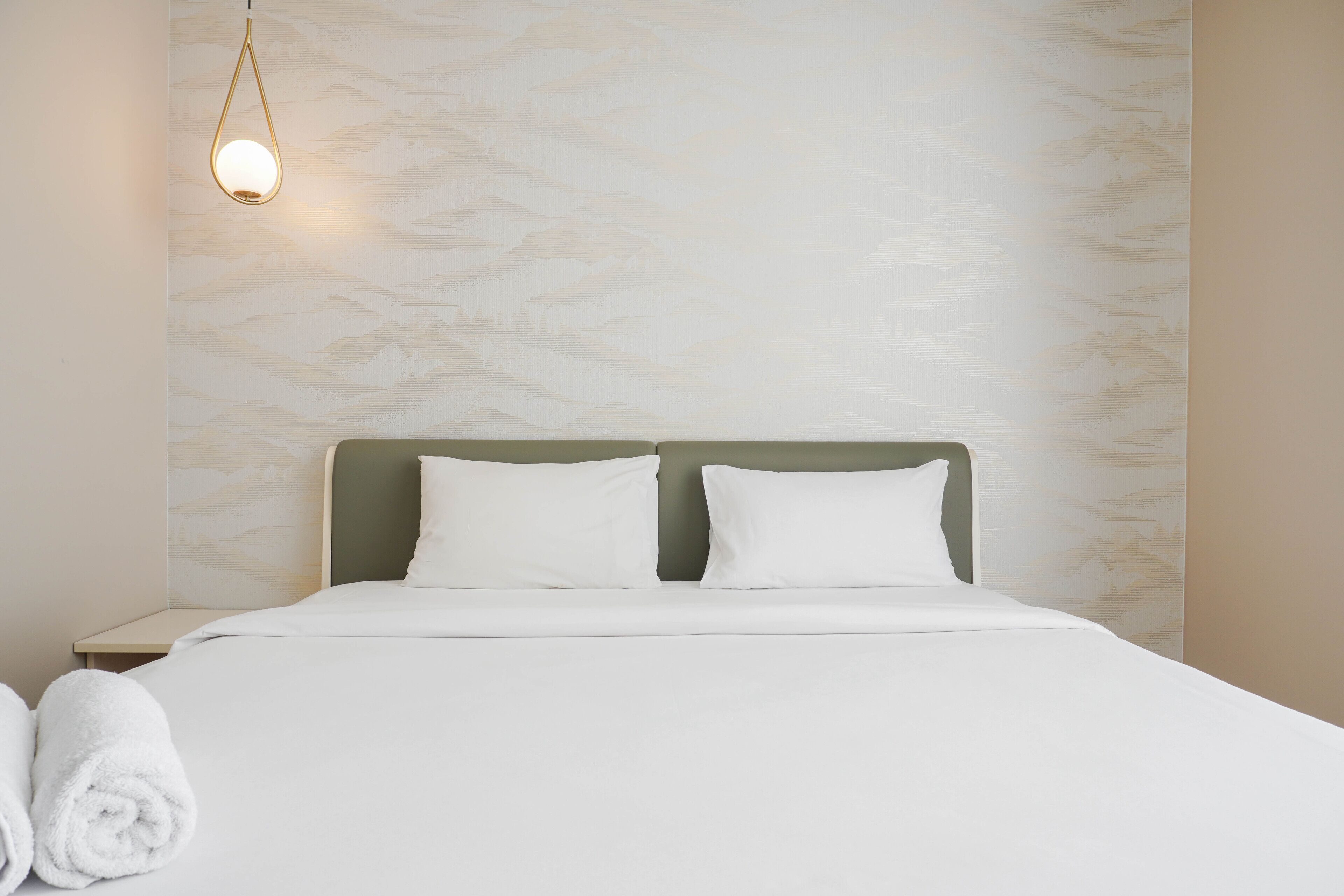 A neatly made bed with white linens and pillows, a hanging light fixture, and a textured wall behind.