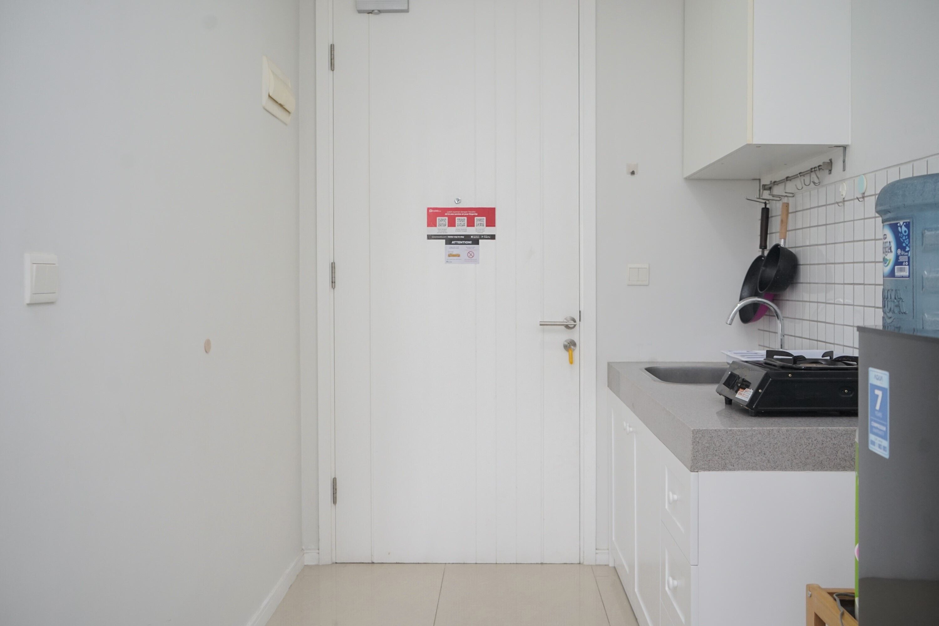A small, clean kitchen with white cabinets, a countertop, and a door with a fire safety sign.