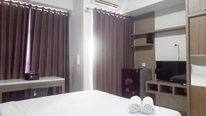 A hotel room with a bed, a desk, a TV, and a wardrobe. - Delightful Luxurious Studio Room at Taman Melati Surabaya Apartment (Surabaya)