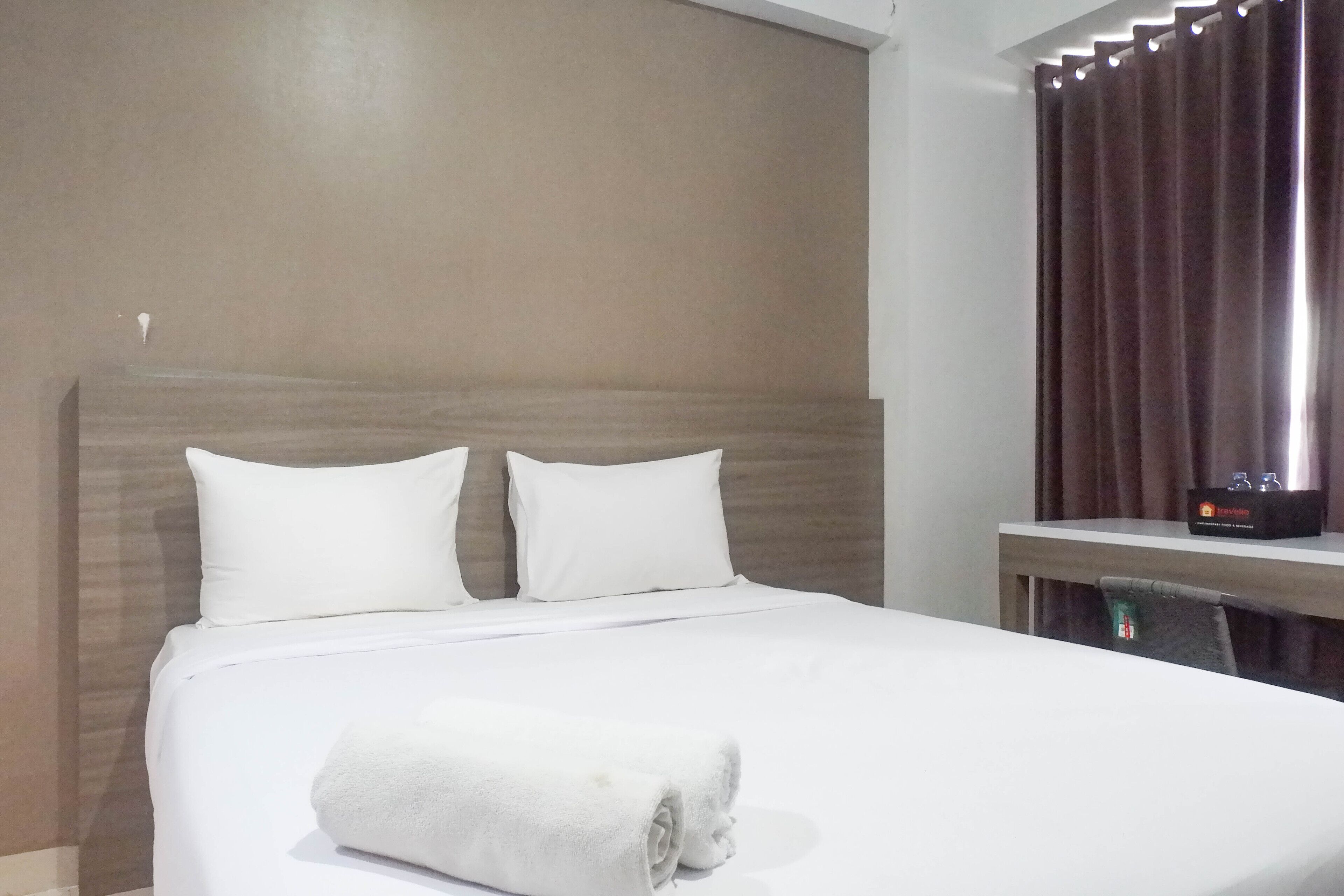 Une chambre d’hôtel avec un lit bien fait, une tête de lit en bois, une table de chevet avec une lampe et une fenêtre avec des rideaux.