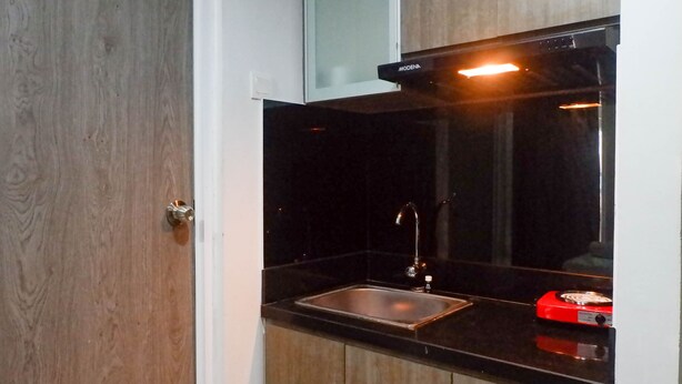 A kitchen with a black countertop, stainless steel sink, and a red appliance. - Delightful Luxurious Studio Room at Taman Melati Surabaya Apartment (Surabaya)