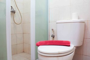 A bathroom with a toilet, a shower, and a toilet paper holder.