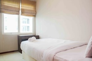 Une chambre à coucher avec un lit, une table de chevet, une fenêtre avec des stores et une vue sur les bâtiments environnants.