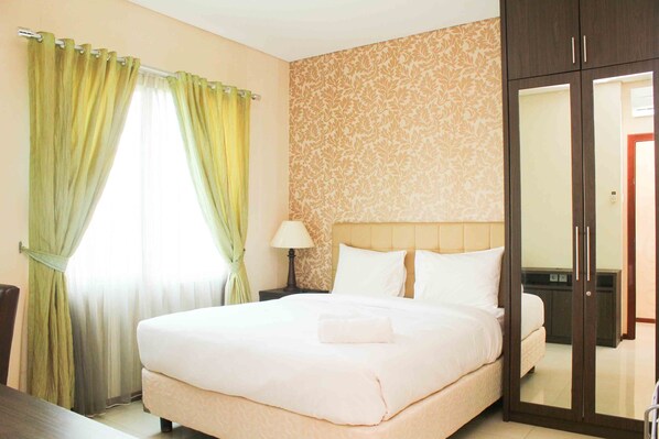 A hotel room with a large bed, a nightstand with a lamp, a wardrobe, and a mirror.