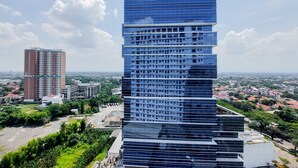 Un immeuble moderne de grande hauteur, doté d’une architecture originale à étages superposés, entouré de verdure et bordé par d’autres bâtiments en arrière-plan.