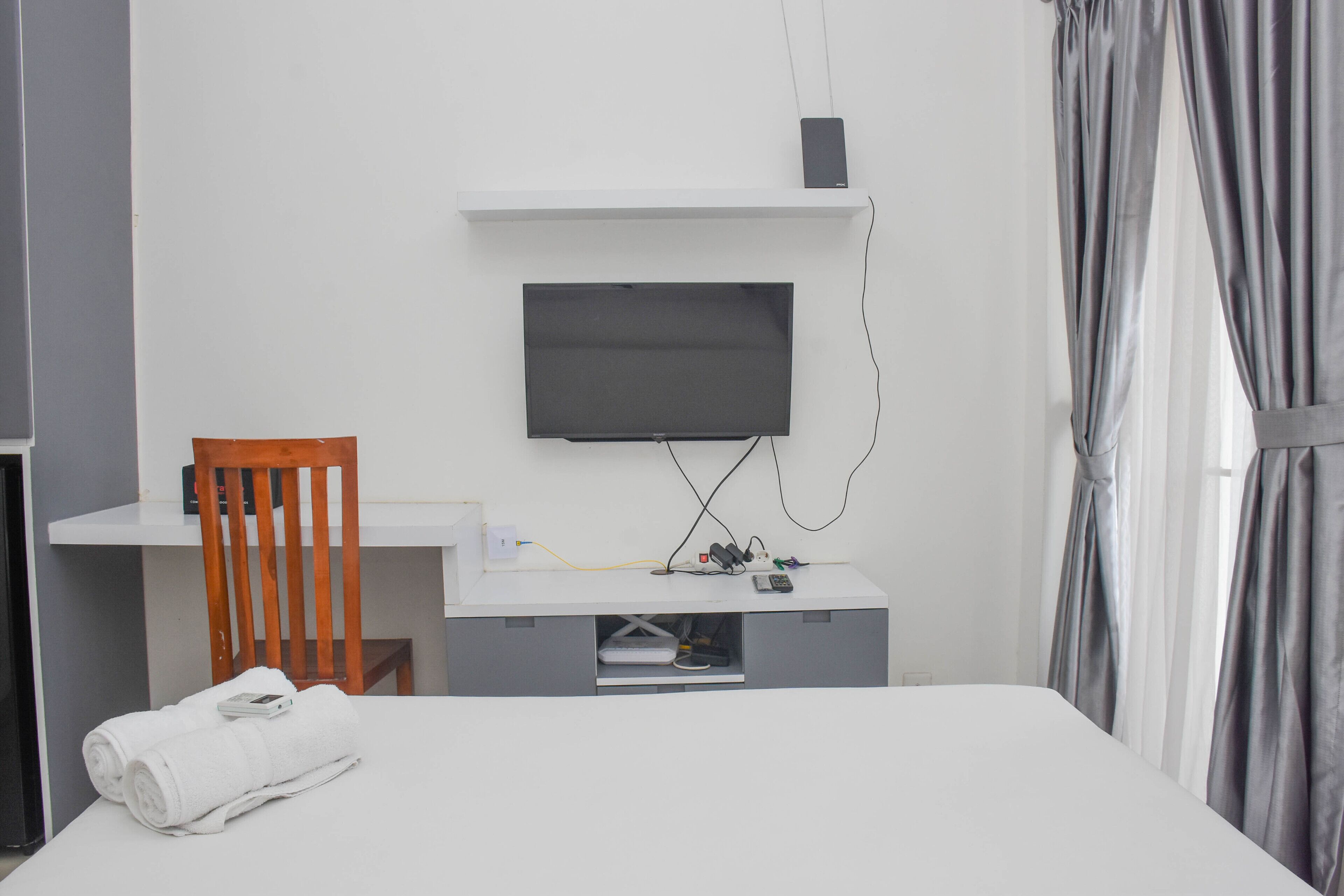 Una habitación de hotel moderna con una cama, un escritorio con televisor de pantalla plana, una silla y un mueble para televisión con un altavoz.