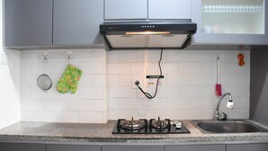 A kitchen with a gas stove, a sink, and a range hood. - Nice and Comfy Studio Apartment at Signature Park Grande (Jakarta)
